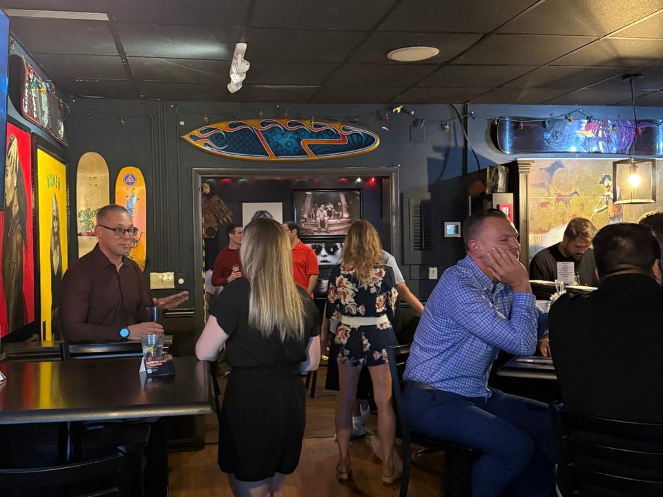 Guests standing and talking in a bar room with surfboards on the wall