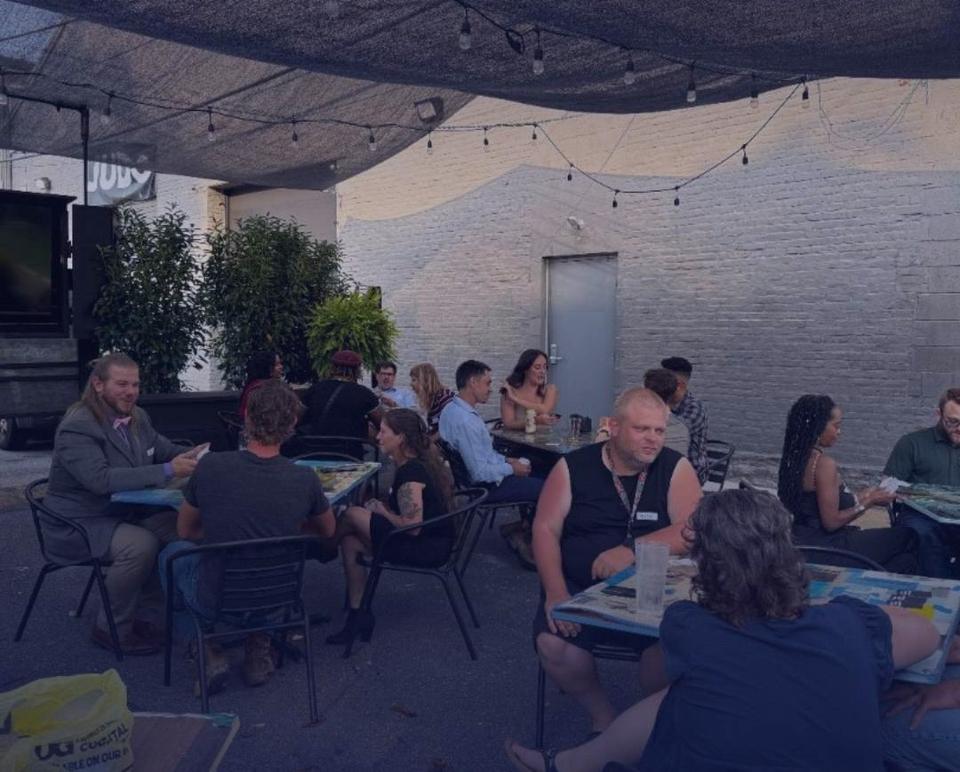 Guests seated at small patio tables under string lights, talking over a table game